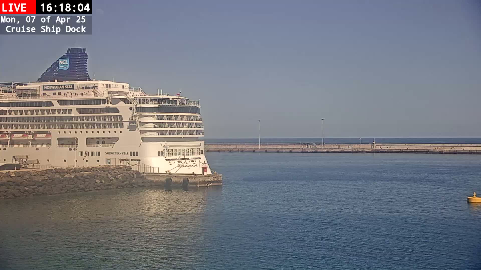 A large cruise ship is docked at a pier on a calm, sunny day.