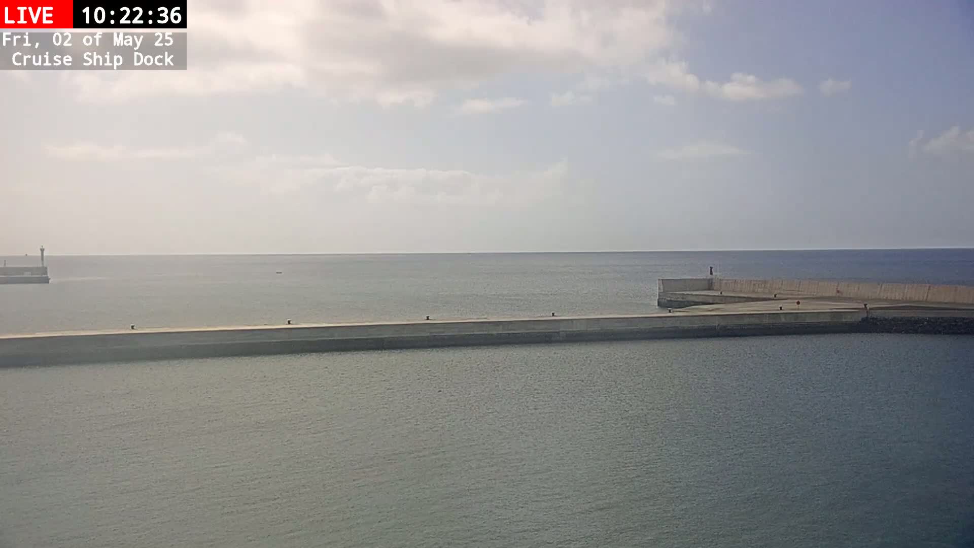 A long concrete pier extends into a calm, gray-blue sea under a partly cloudy sky.