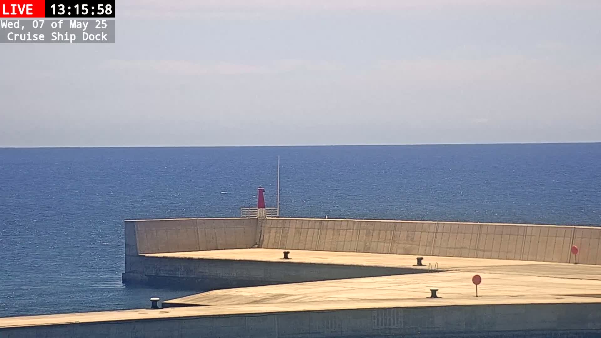 A concrete cruise ship dock extends into a calm blue sea under a mostly clear sky.