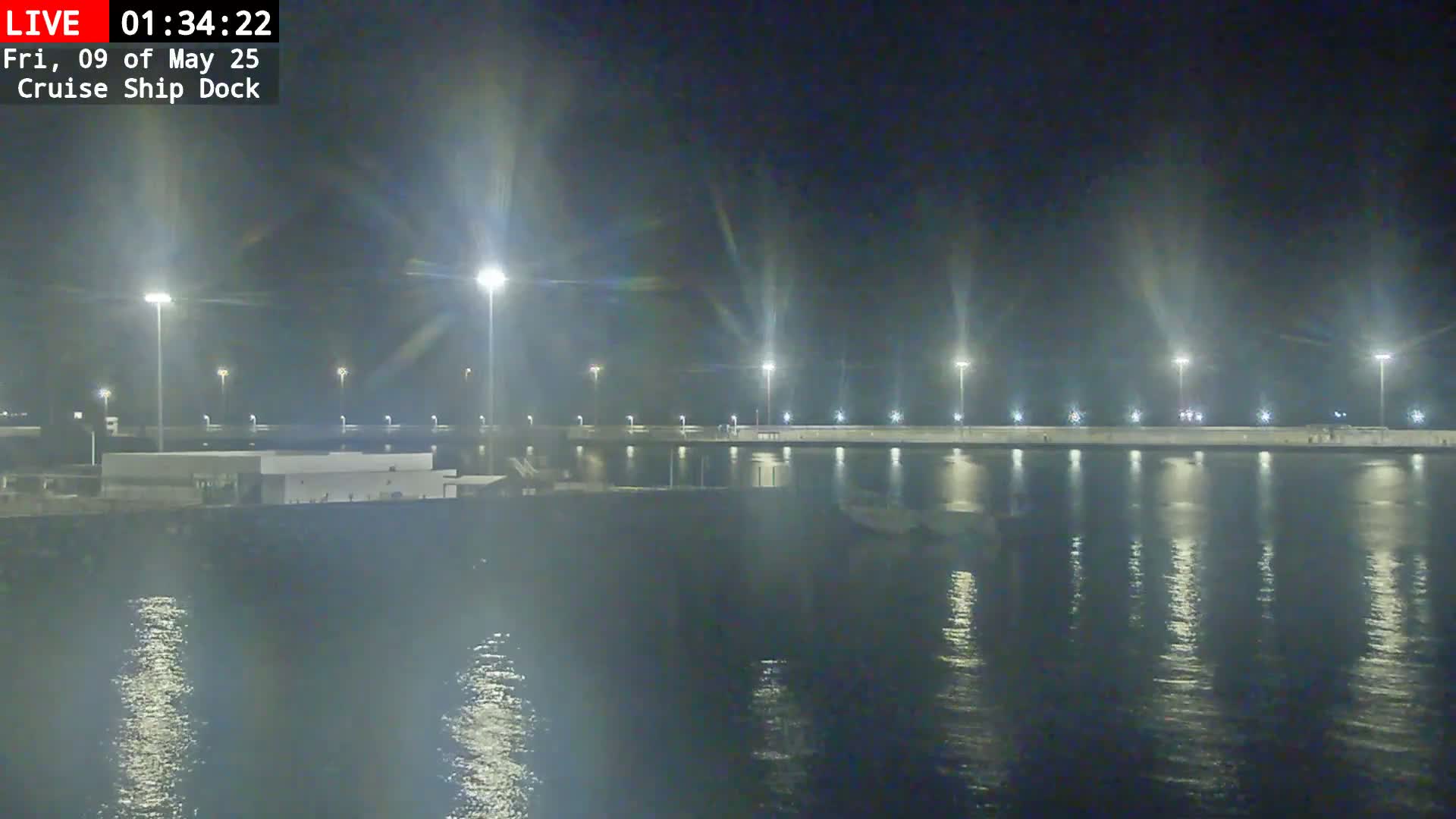 A nighttime view of a brightly lit cruise ship dock and calm water reflecting the lights.