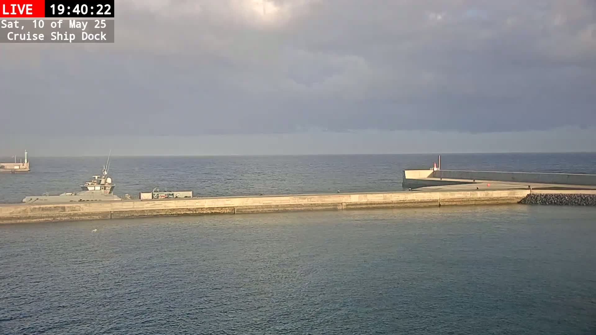 A ship is docked at a concrete pier on a calm sea under a mostly cloudy sky.