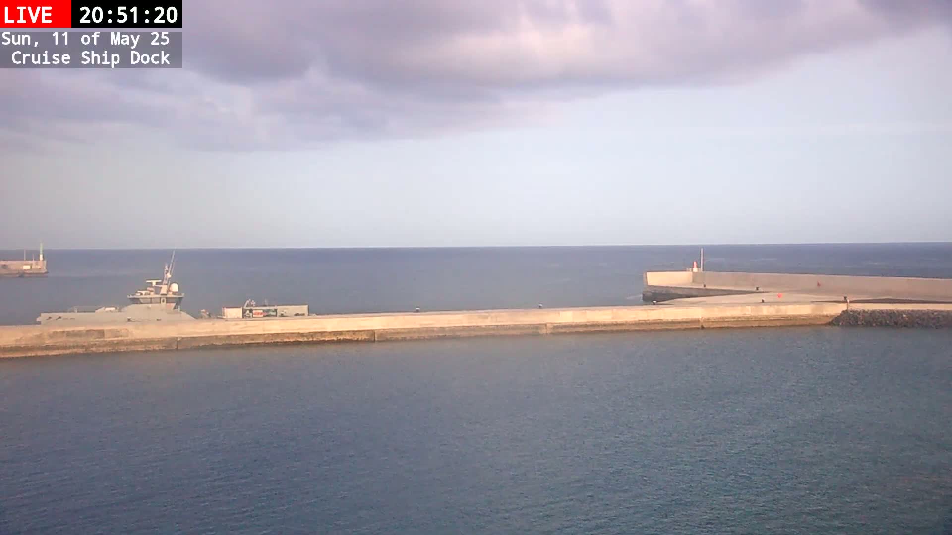 A ship is docked at a concrete pier on a calm sea under a partly cloudy sky.