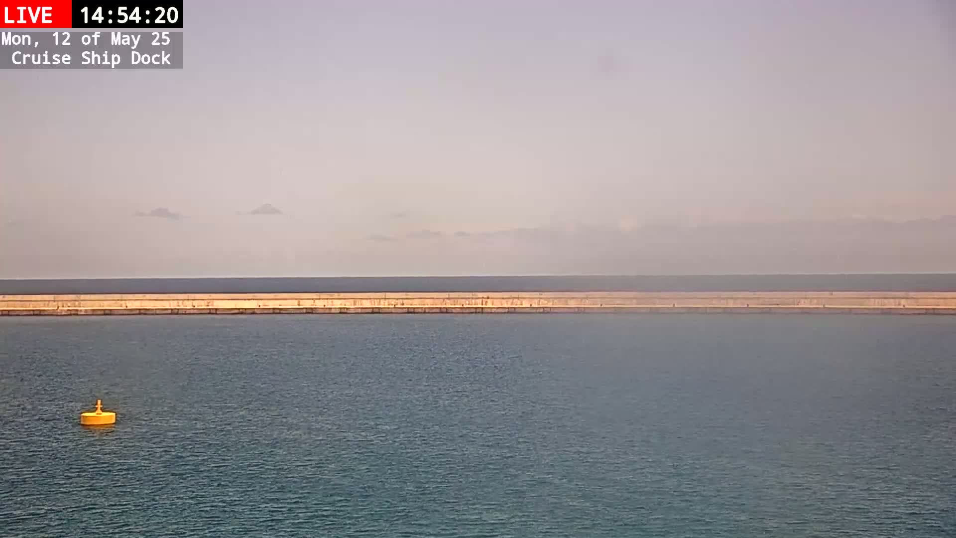 A long, low seawall stretches across the frame, separating calmer inner waters from a hazy, distant ocean under a pale sky.