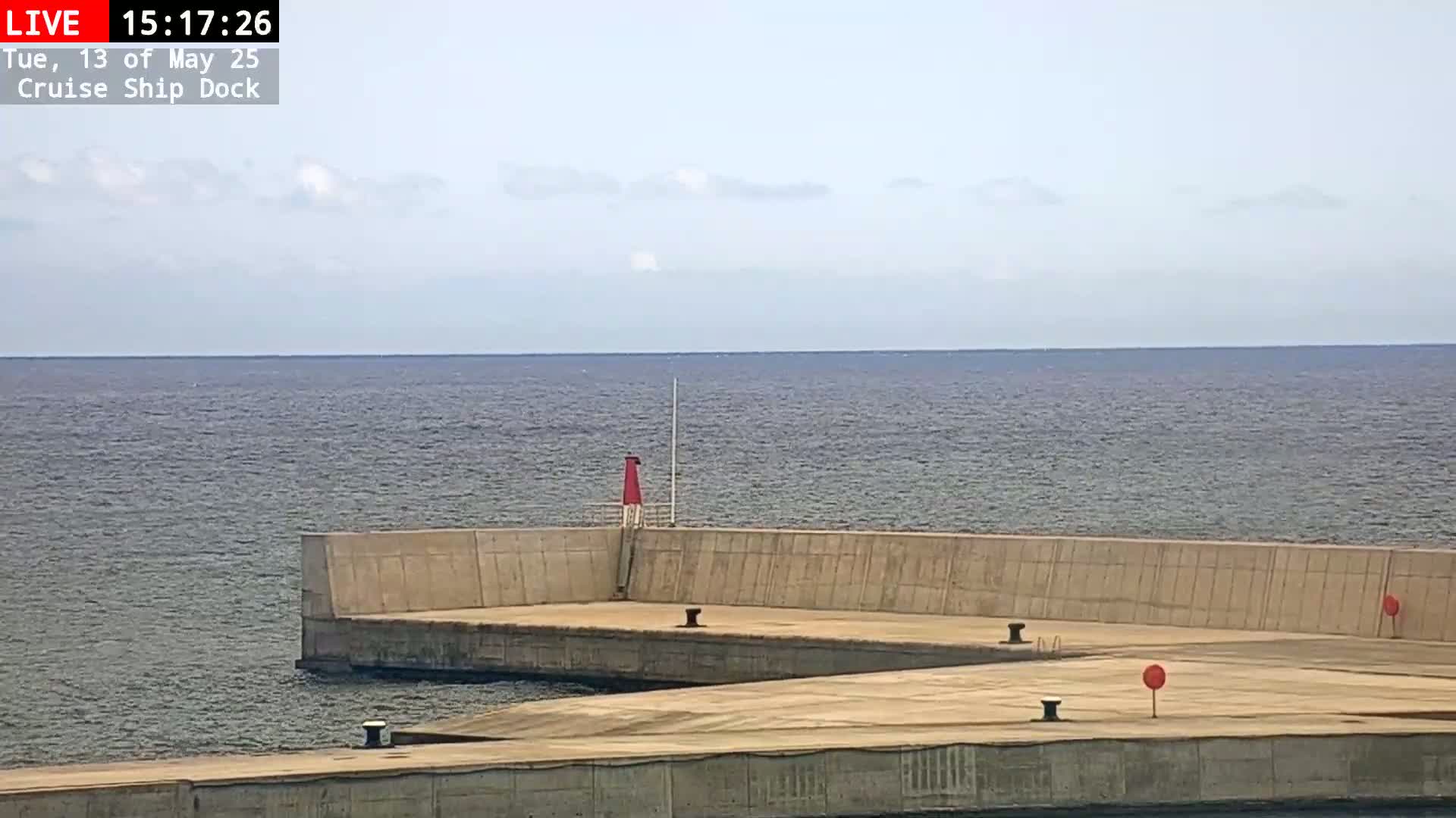 A mostly calm sea is visible beyond a concrete cruise ship dock on a partly cloudy day.