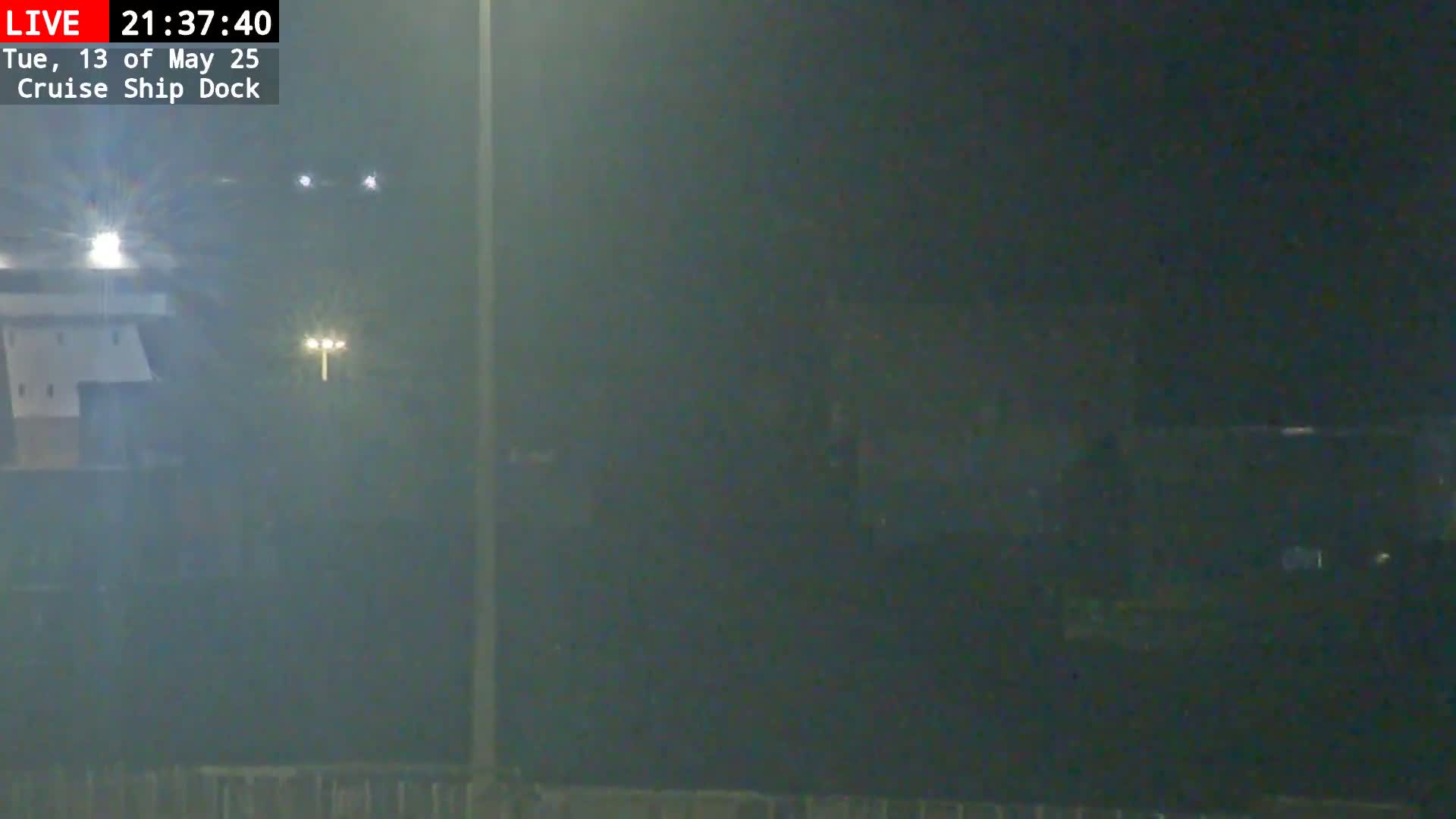 A nighttime, foggy view of a cruise ship dock with faint lights visible in the distance.