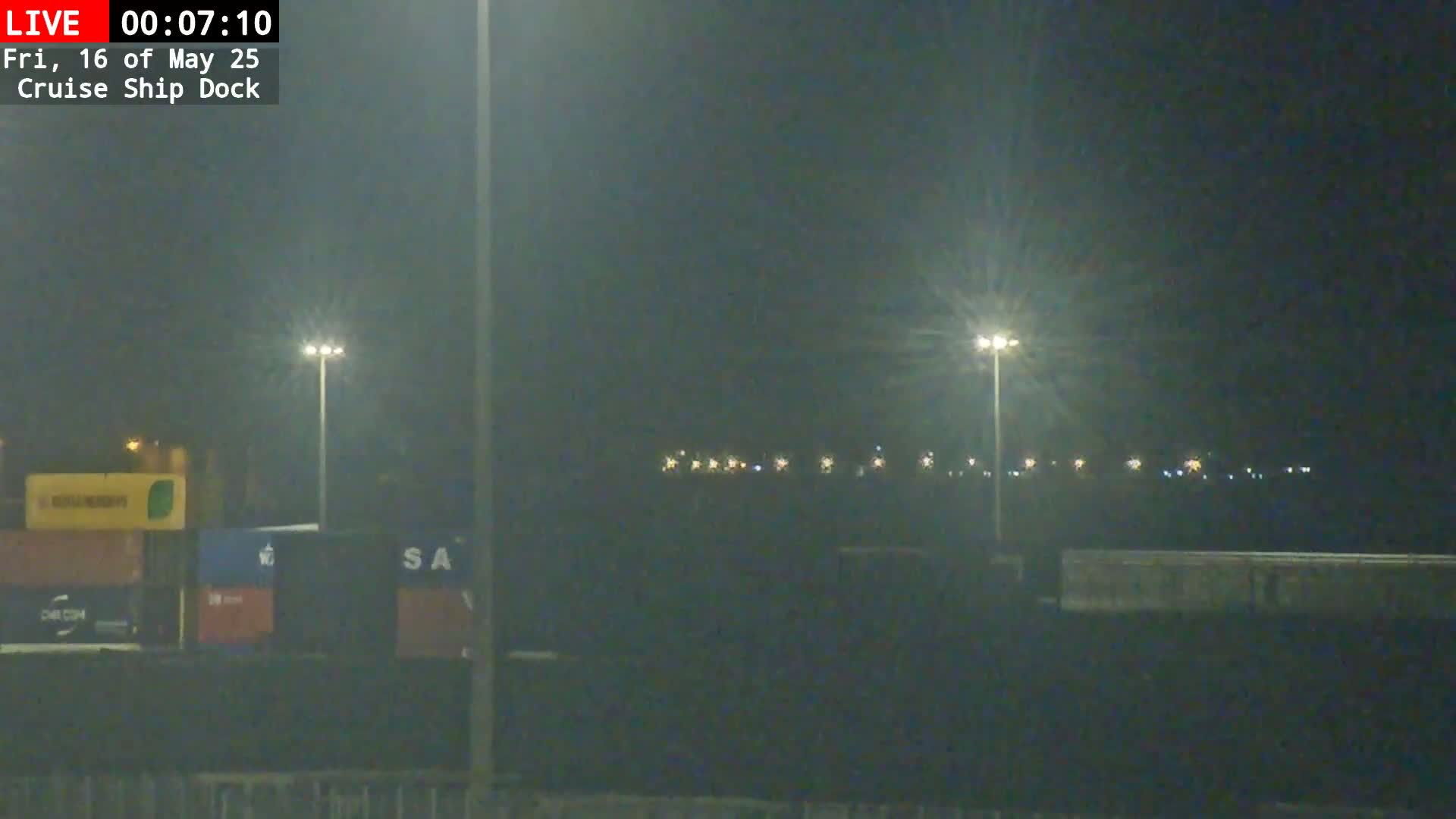 At night, under hazy conditions, illuminated shipping containers and tall lights are visible at a cruise ship dock.