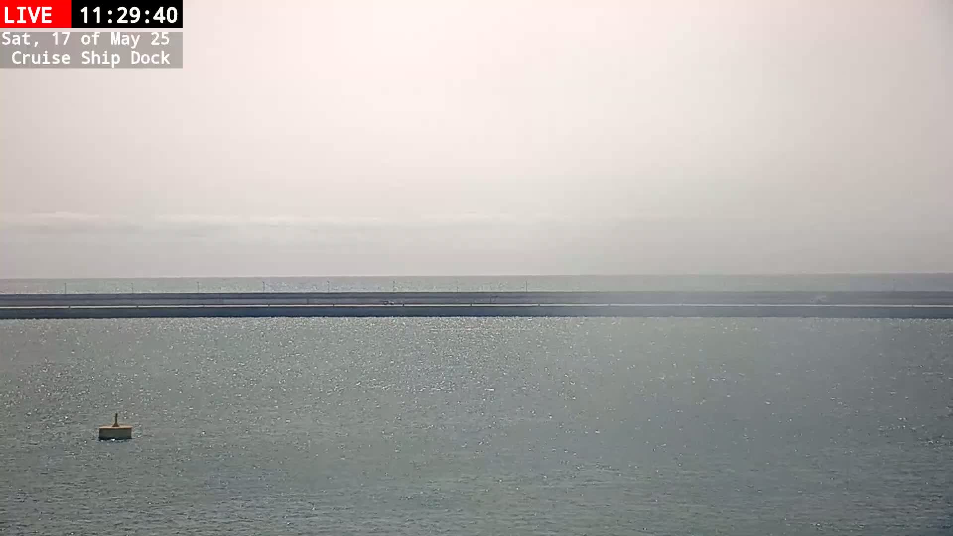 A hazy day reveals a calm body of water with a distant shoreline and a small buoy in the foreground.