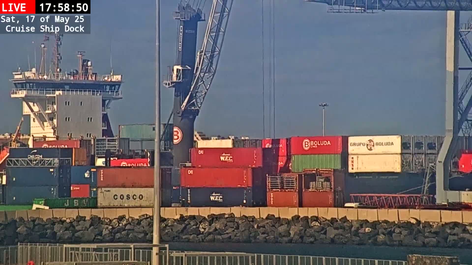 A cargo ship and a container crane are visible at a dock on a sunny day.