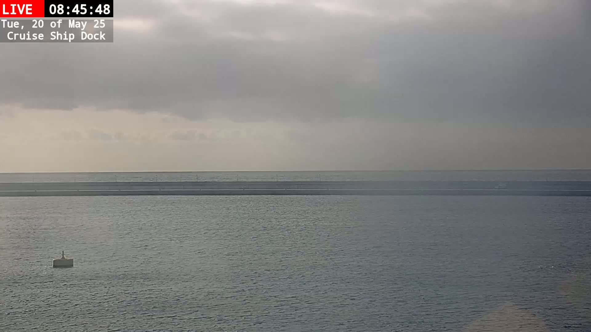 A calm body of water with a long, low structure in the distance under an overcast sky.