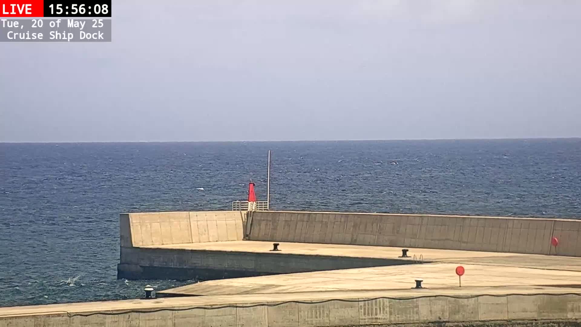 A concrete cruise ship dock extends into a calm, blue ocean under a clear sky.