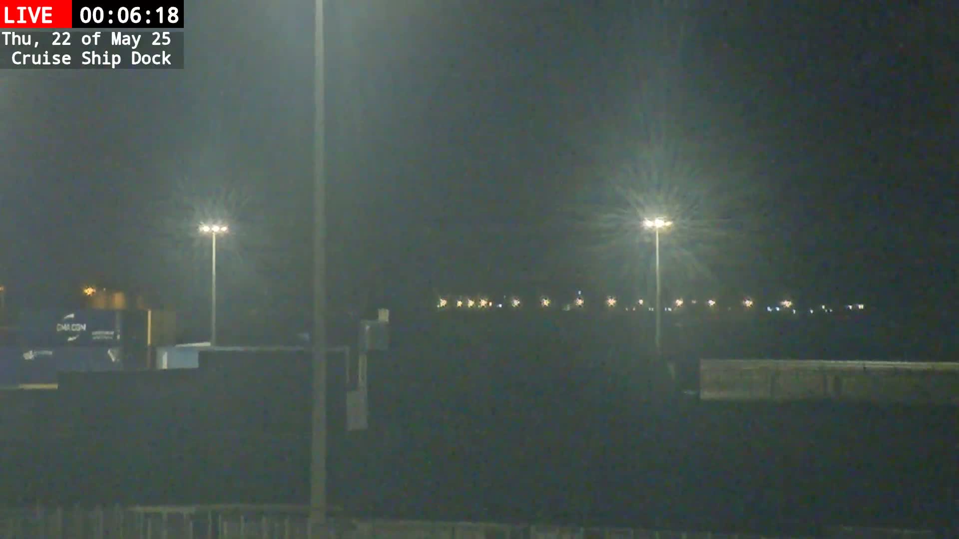 A nighttime view of a dimly lit dock area with several tall lights illuminating the scene under a dark, overcast sky.