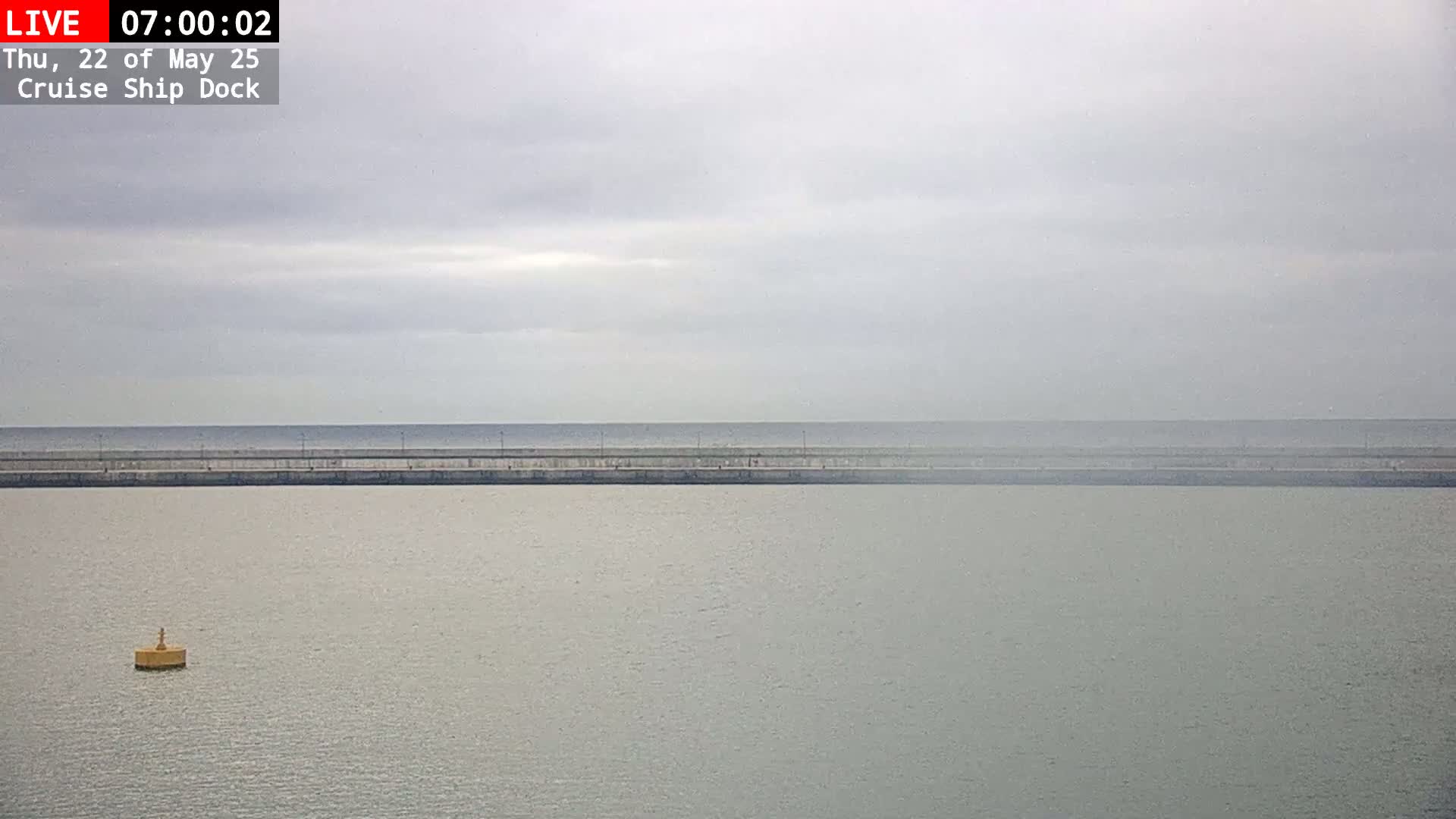 A calm body of water is seen behind a long, low seawall under an overcast sky.