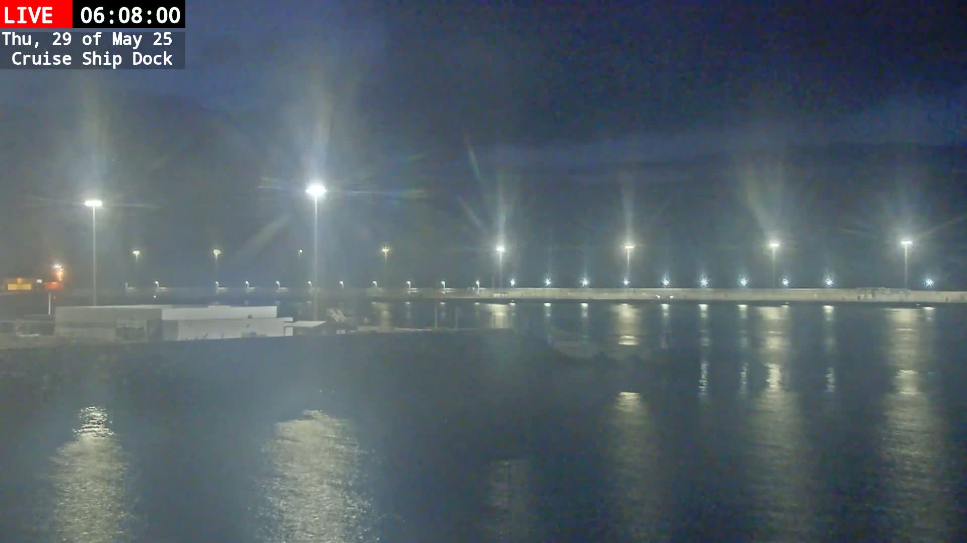 A nighttime view of a brightly lit cruise ship dock reflecting in calm water under a dark sky.