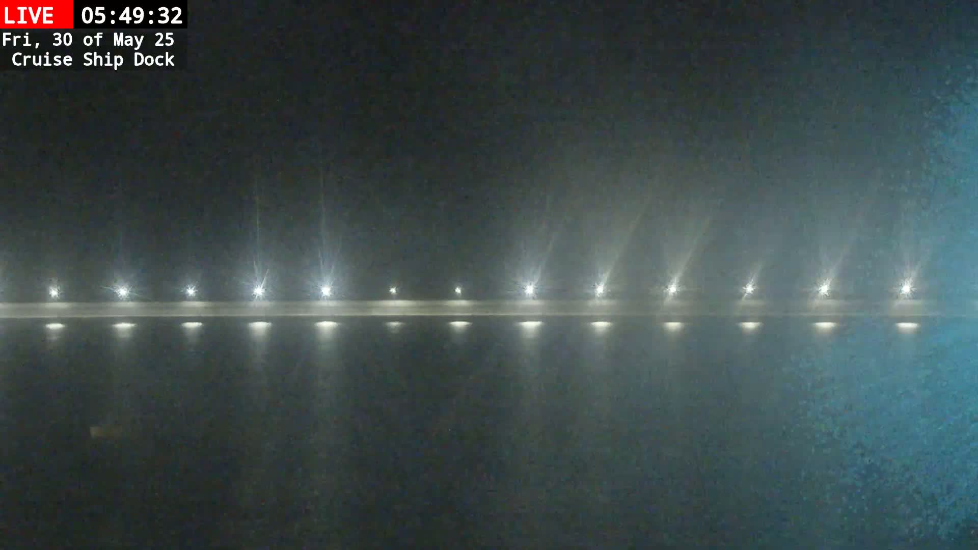 A long, low structure with evenly spaced lights is visible in the fog at night.