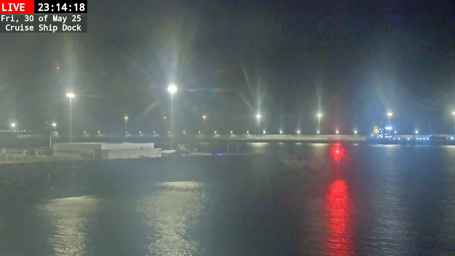 A nighttime view of a cruise ship dock with a large ship docked, illuminated by bright lights, and calm water reflecting the lights.