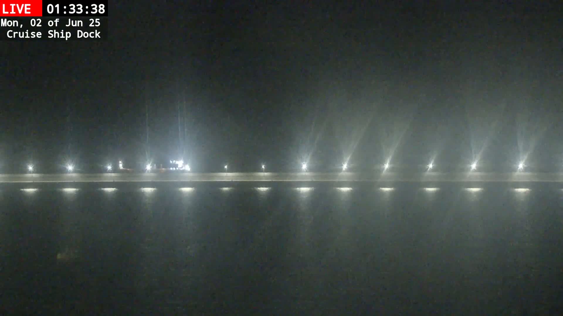 A nighttime, foggy view shows a long, illuminated dock with a few vehicles parked on it.