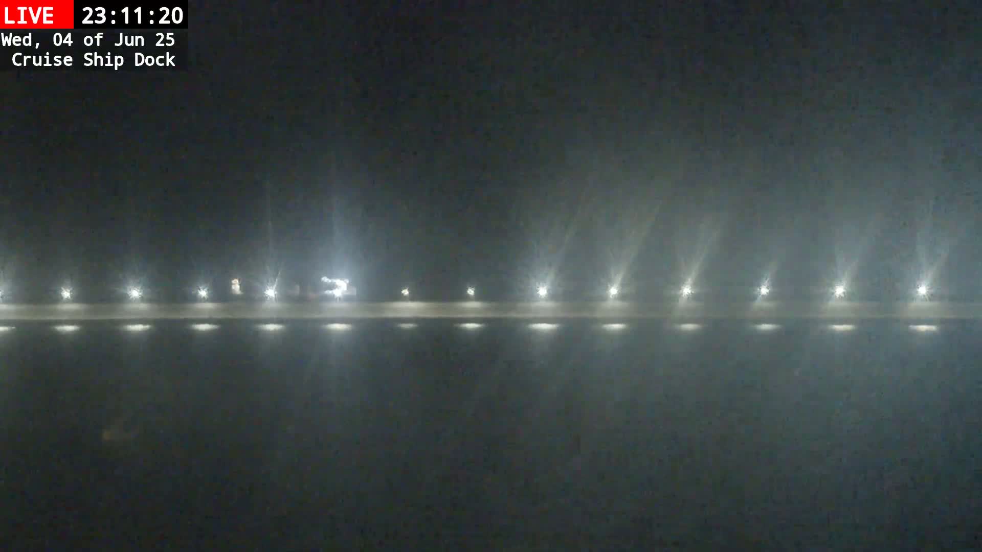 A nighttime, foggy view of a brightly lit dock with several lights along its length.