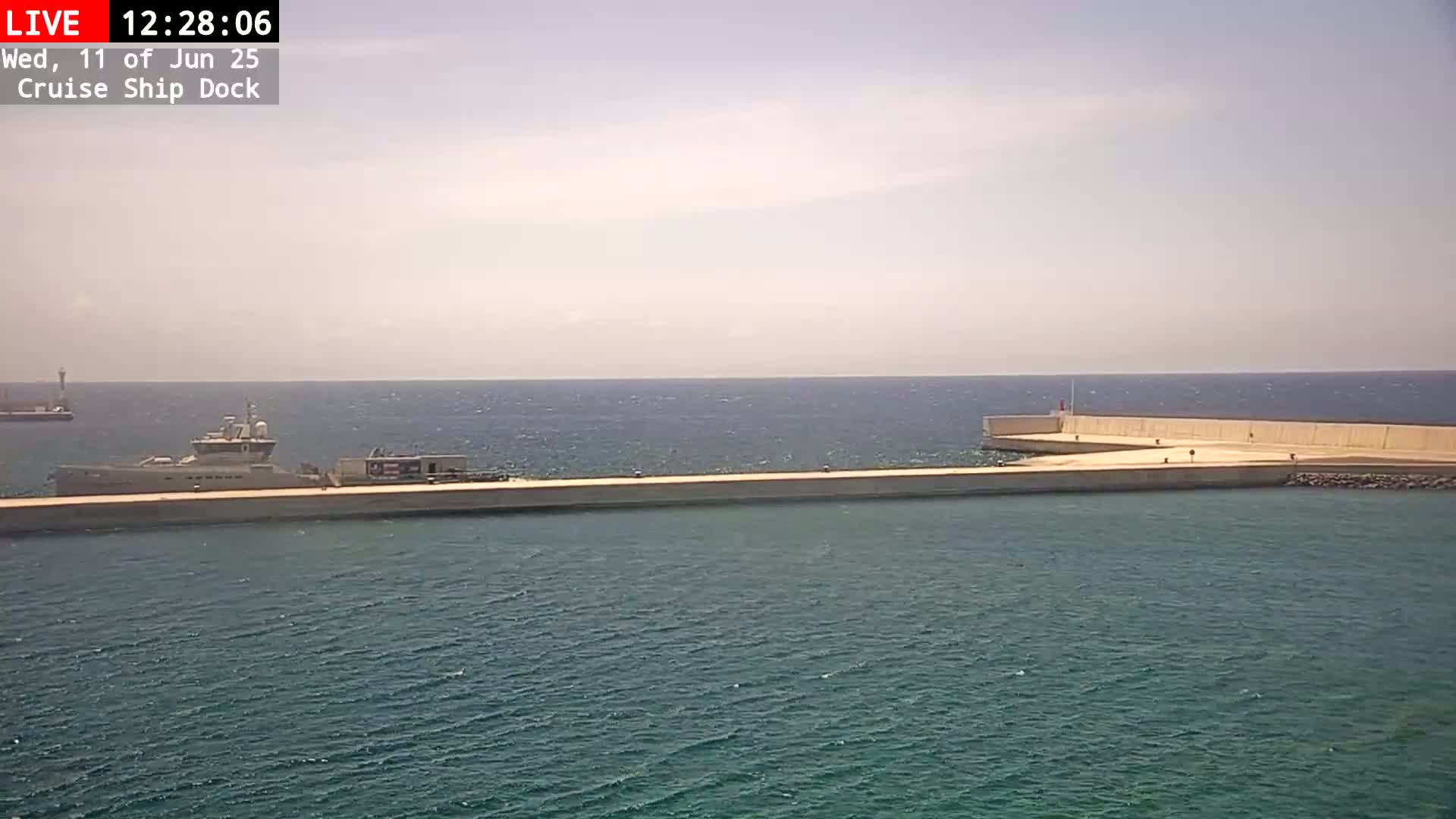 A large ship is docked at a concrete pier on a calm, sunny day.
