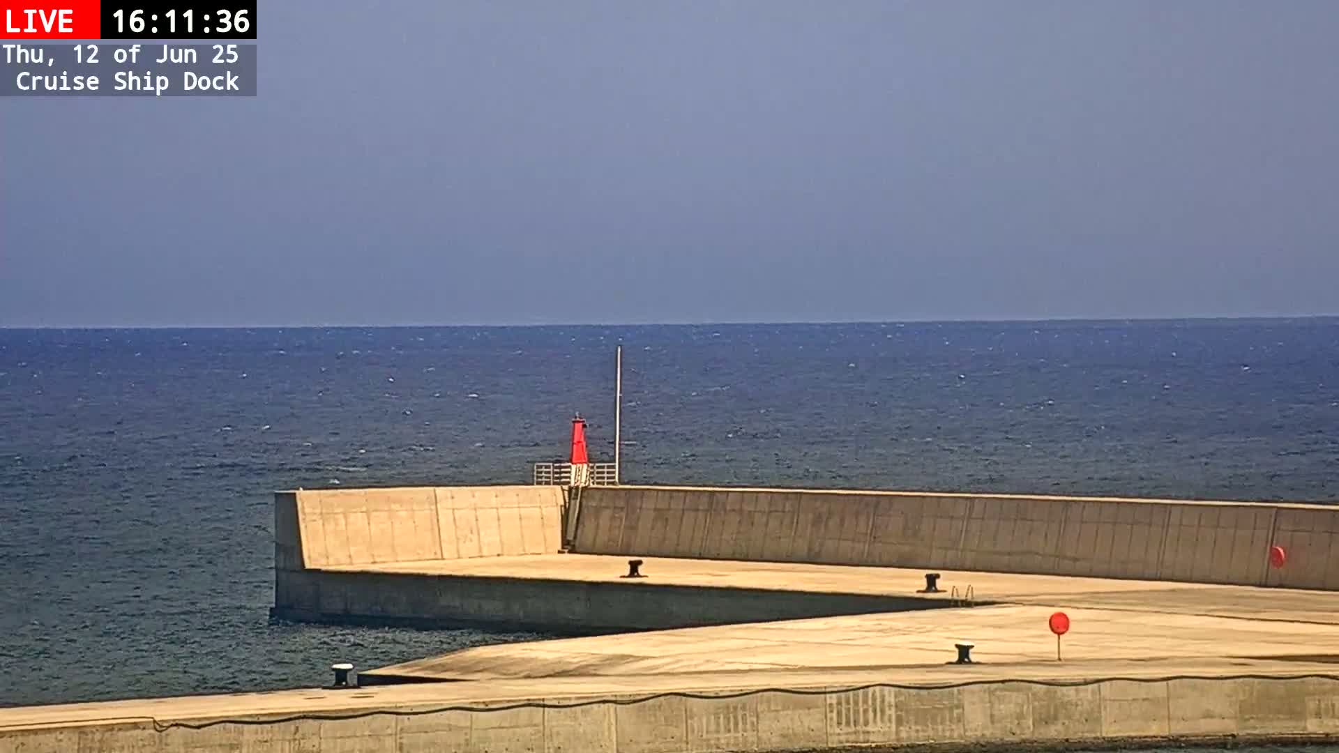 A concrete cruise ship dock extends into a calm, blue ocean under a clear sky.