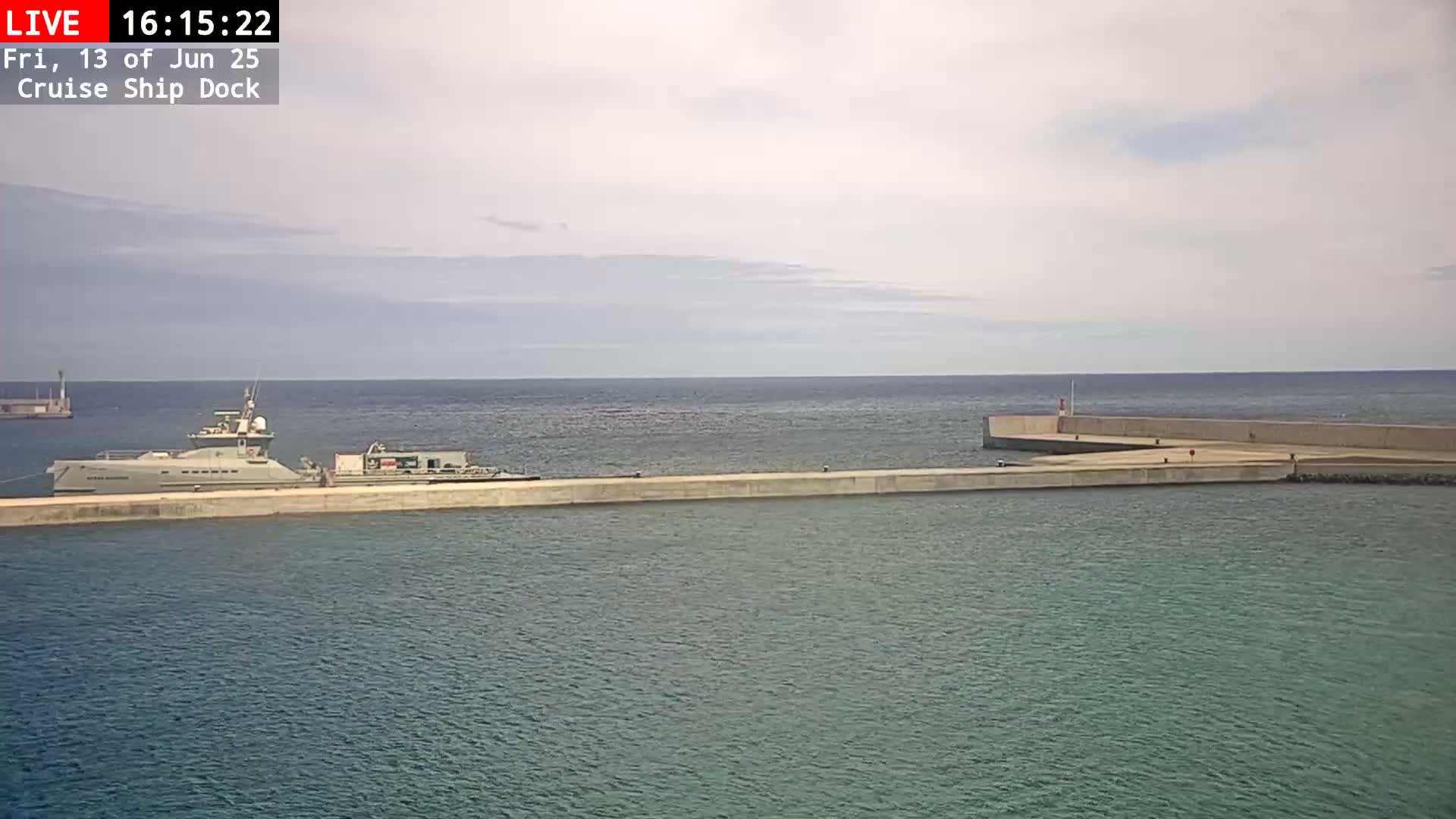 A large ship is docked at a concrete pier on a calm, overcast day.