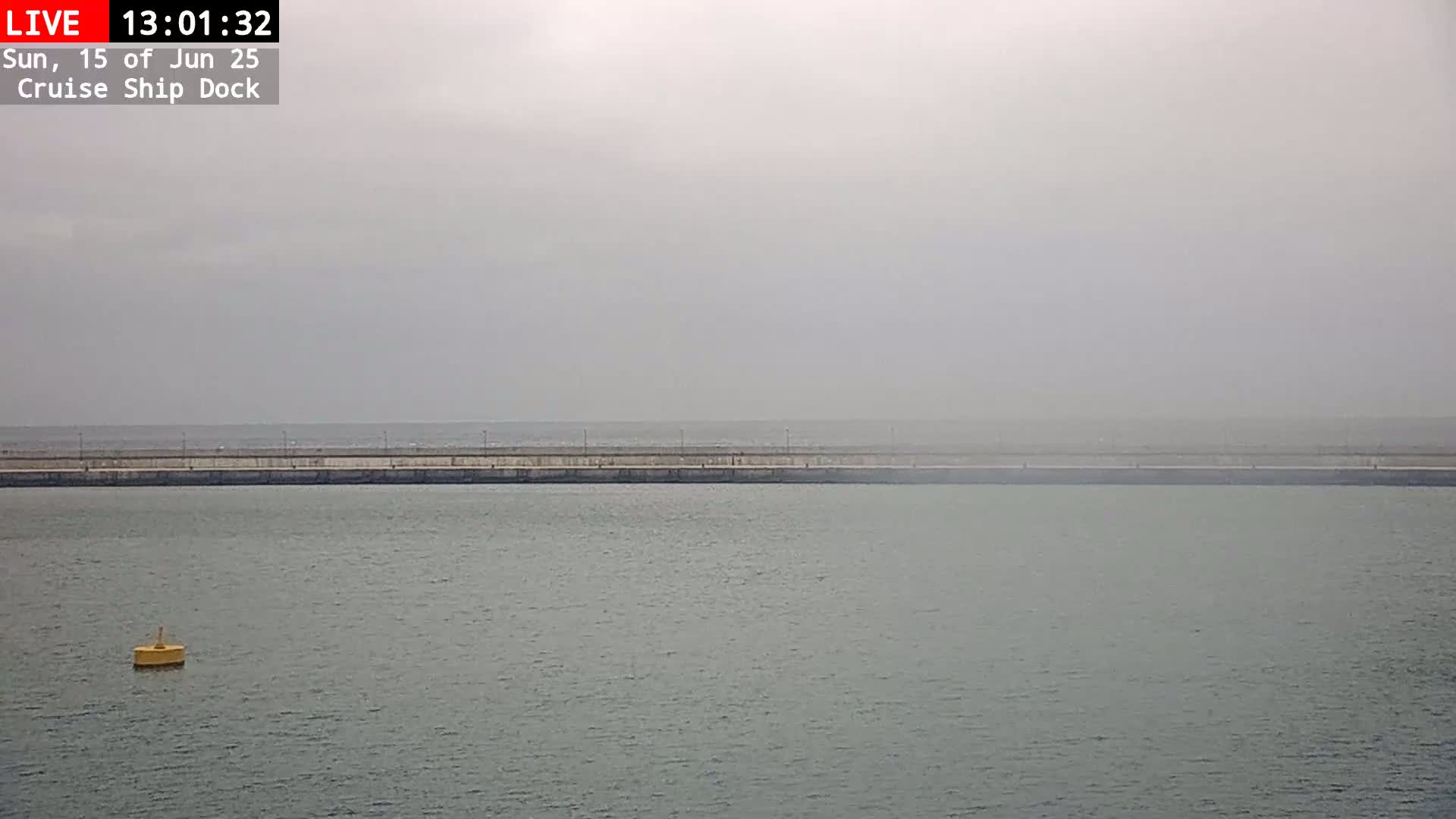 A long, gray seawall stretches across a foggy, gray body of water, with a single yellow buoy in the foreground.
