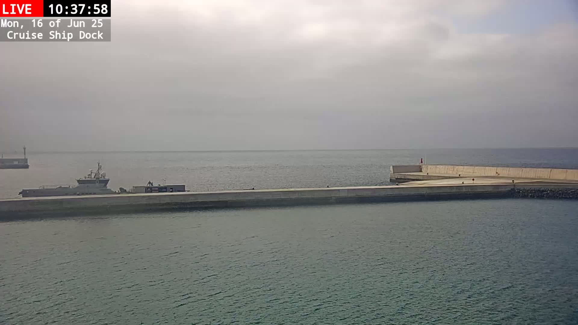 A cruise ship dock on an overcast day shows a vessel moored at the dock and calm water.