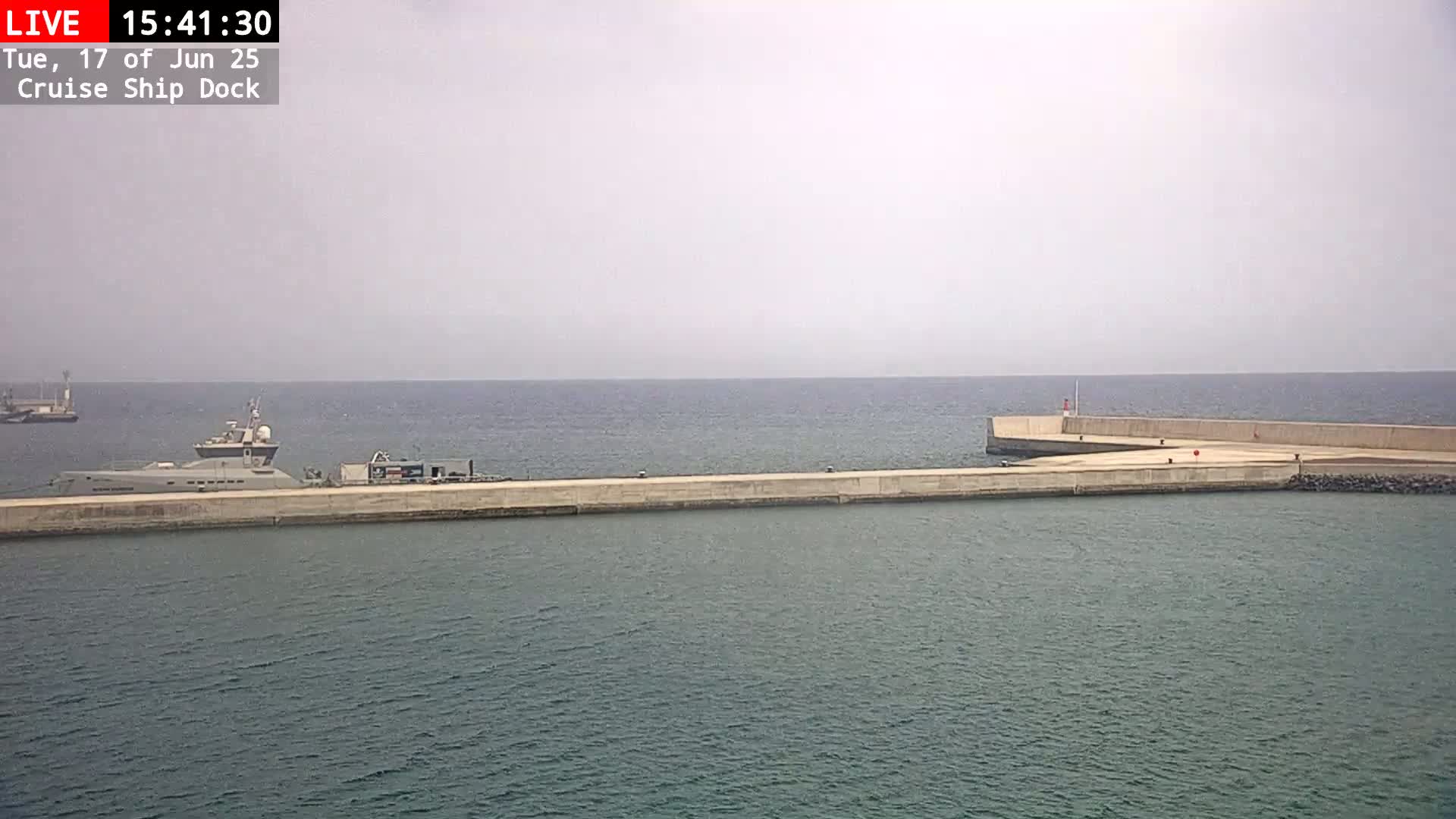 A large ship is docked at a concrete pier on a calm, overcast day.