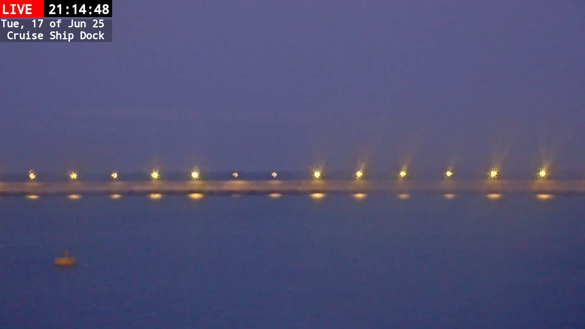 A long, dark pier with evenly spaced lights is visible on a calm, dark-blue body of water at twilight.