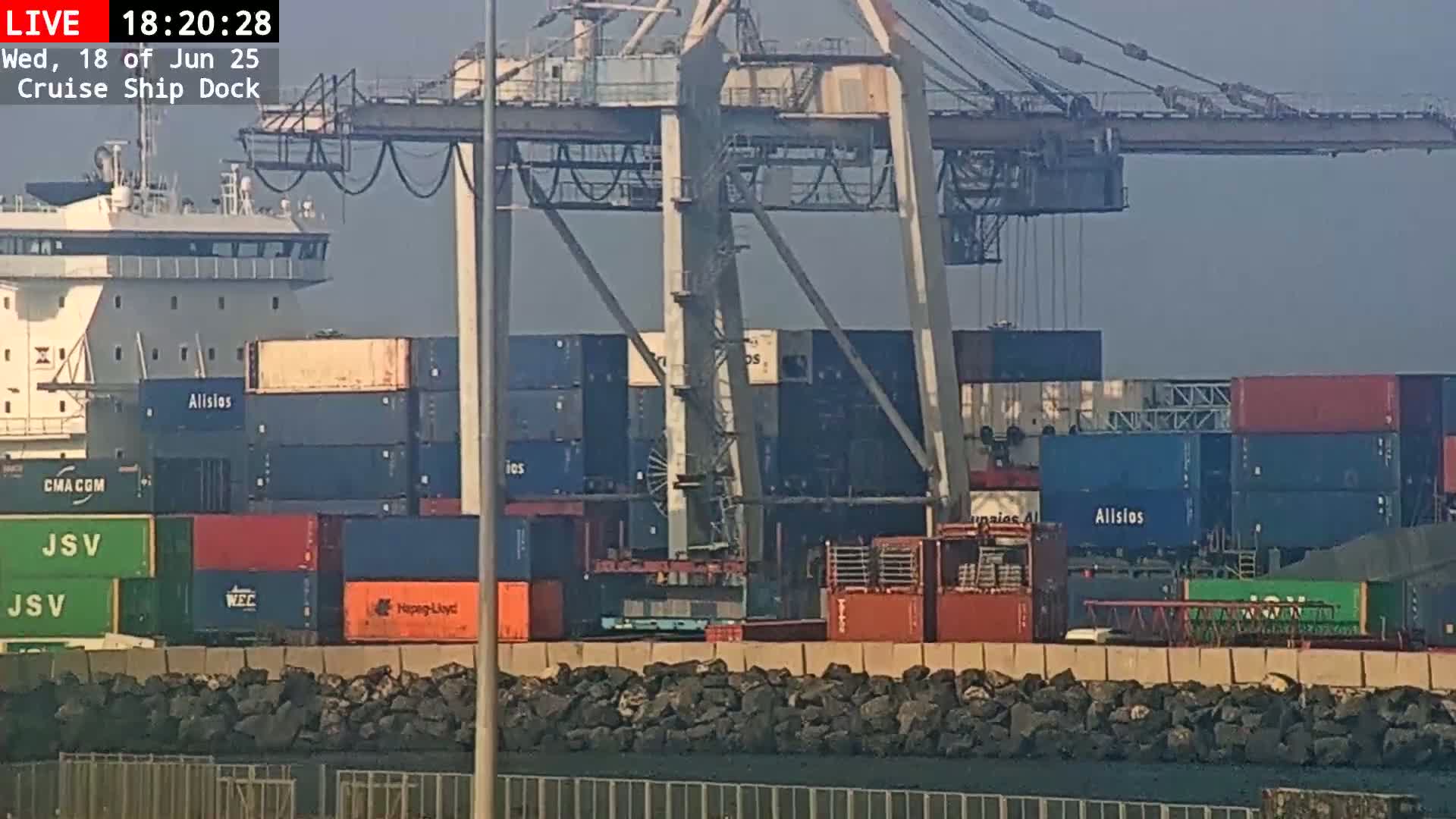 A container ship is docked at a port under hazy, daytime conditions, with large gantry cranes overhead.