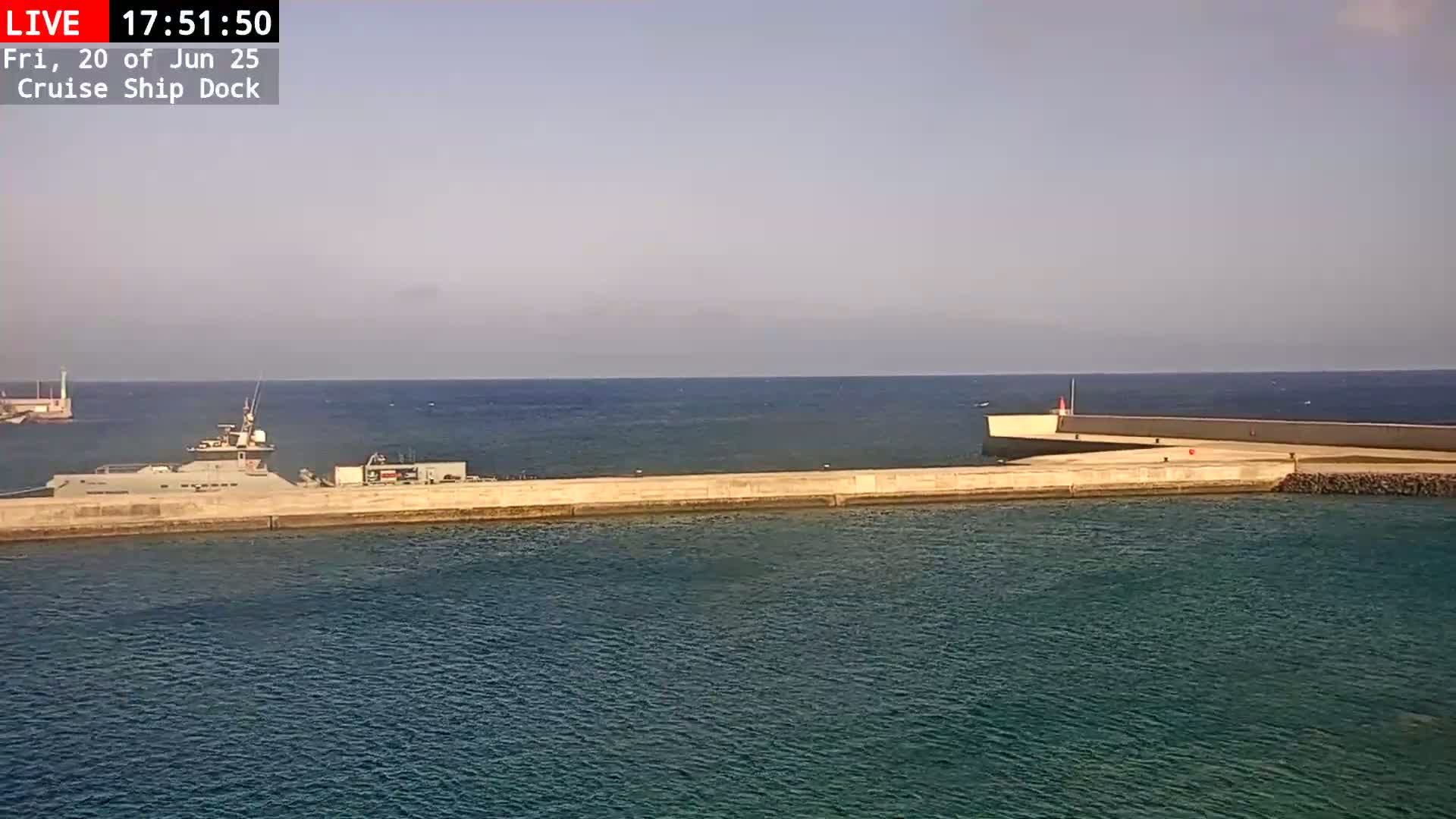 A gray naval ship is docked at a concrete pier on a calm, sunny day.