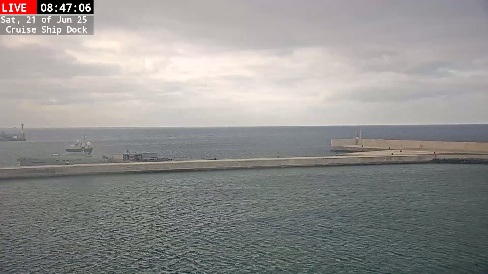A ship is docked at a concrete pier on a calm, overcast day.