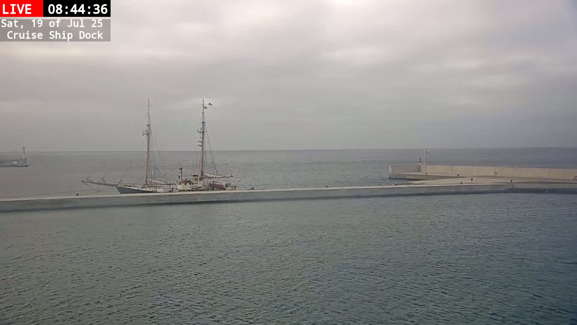 A large sailing ship is docked at a concrete pier on an overcast day.