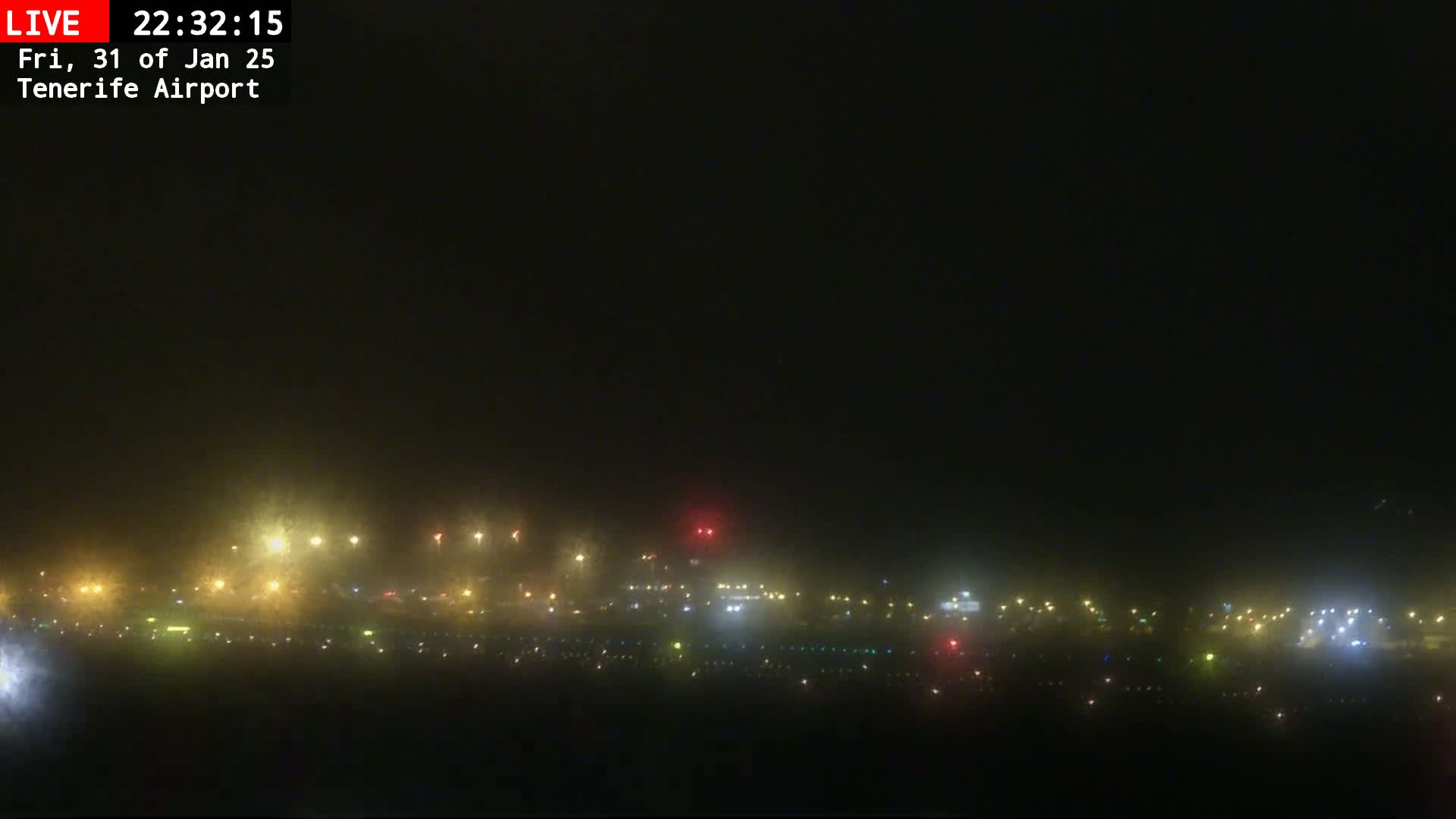 A nighttime view of an airport runway and surrounding buildings obscured by fog.