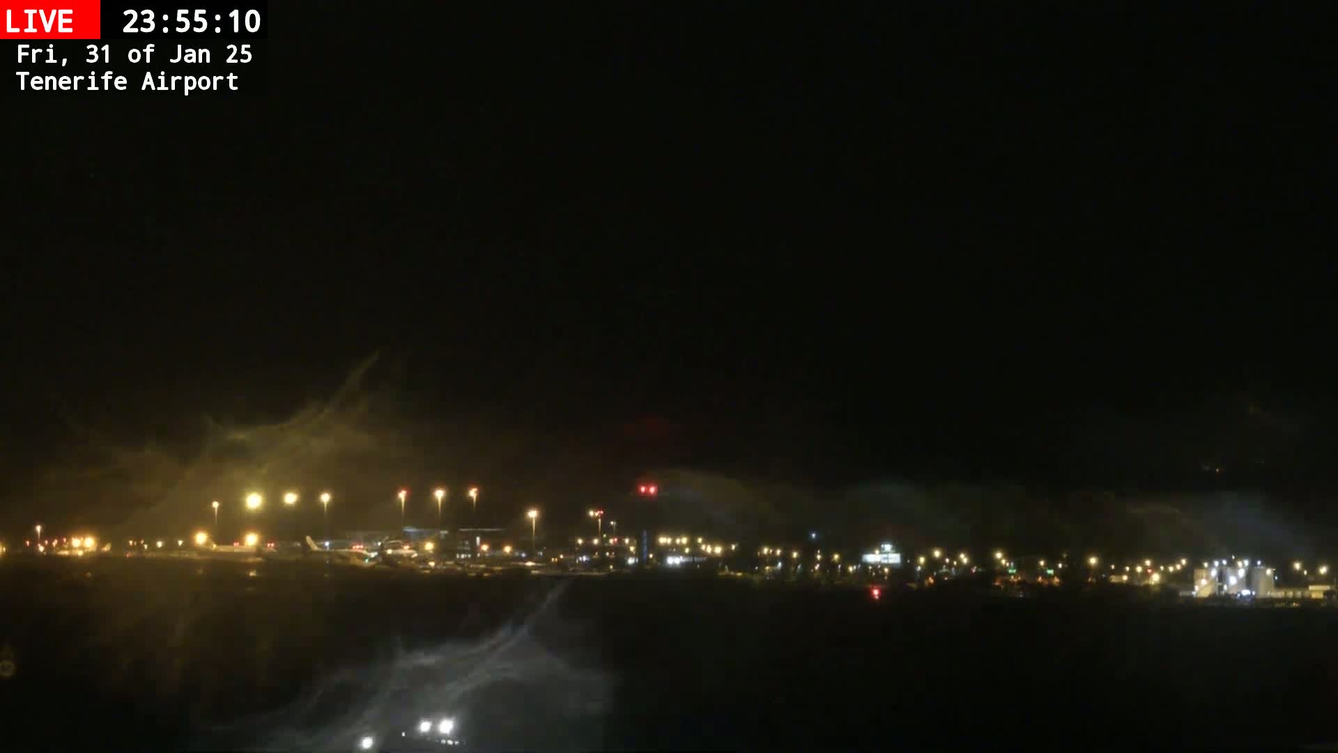 A nighttime view of an airport runway with lights illuminated, partially obscured by a hazy or foggy atmosphere.