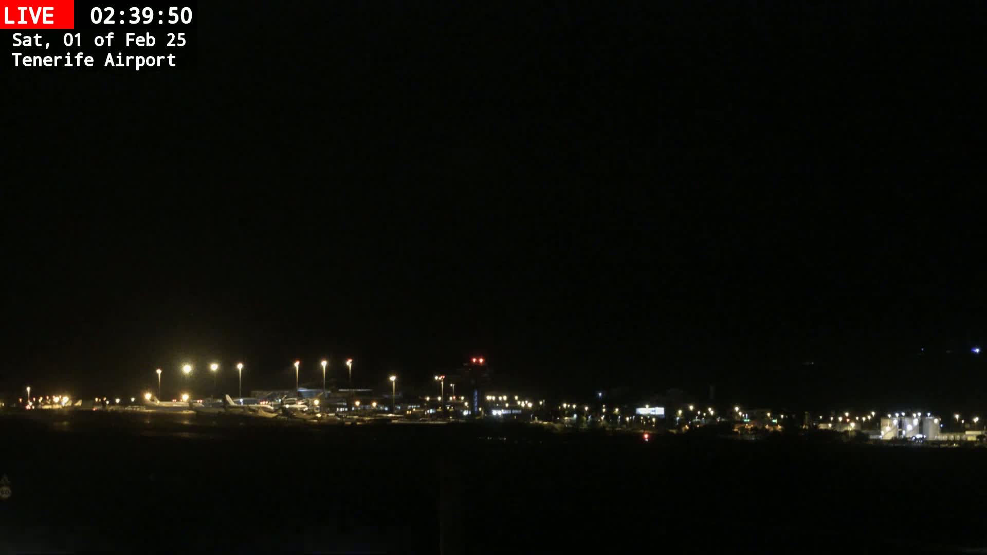 A nighttime view of an airport tarmac with several airplanes and illuminated buildings under a dark, clear sky.