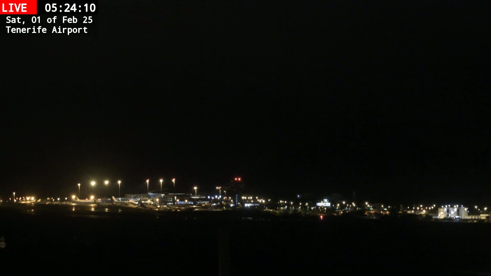 A nighttime, dark view of an airport tarmac with several planes and lights visible under a clear, dark sky.