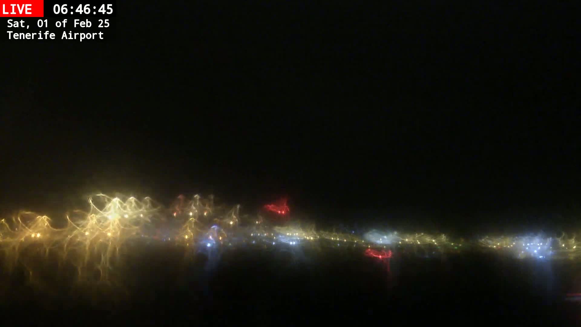 A nighttime view shows a blurry, hazy line of multicolored lights across a dark sky.