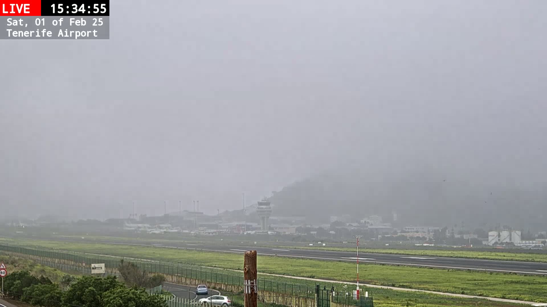 A foggy view of an airport runway, with a control tower visible in the distance.
