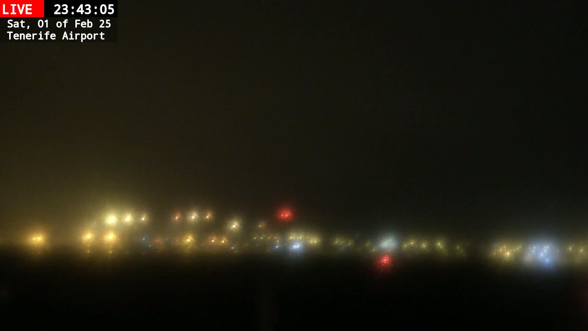 A foggy night scene shows a blurry line of multicolored lights in the distance.