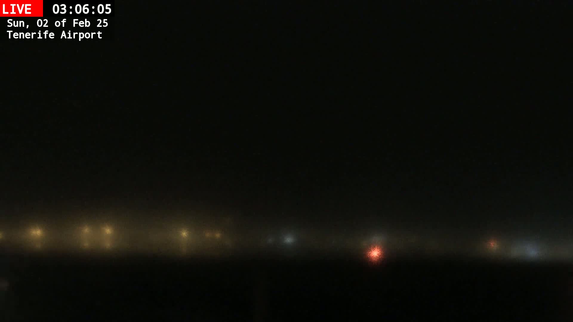 A line of dimly lit lights is barely visible through a thick fog at night.