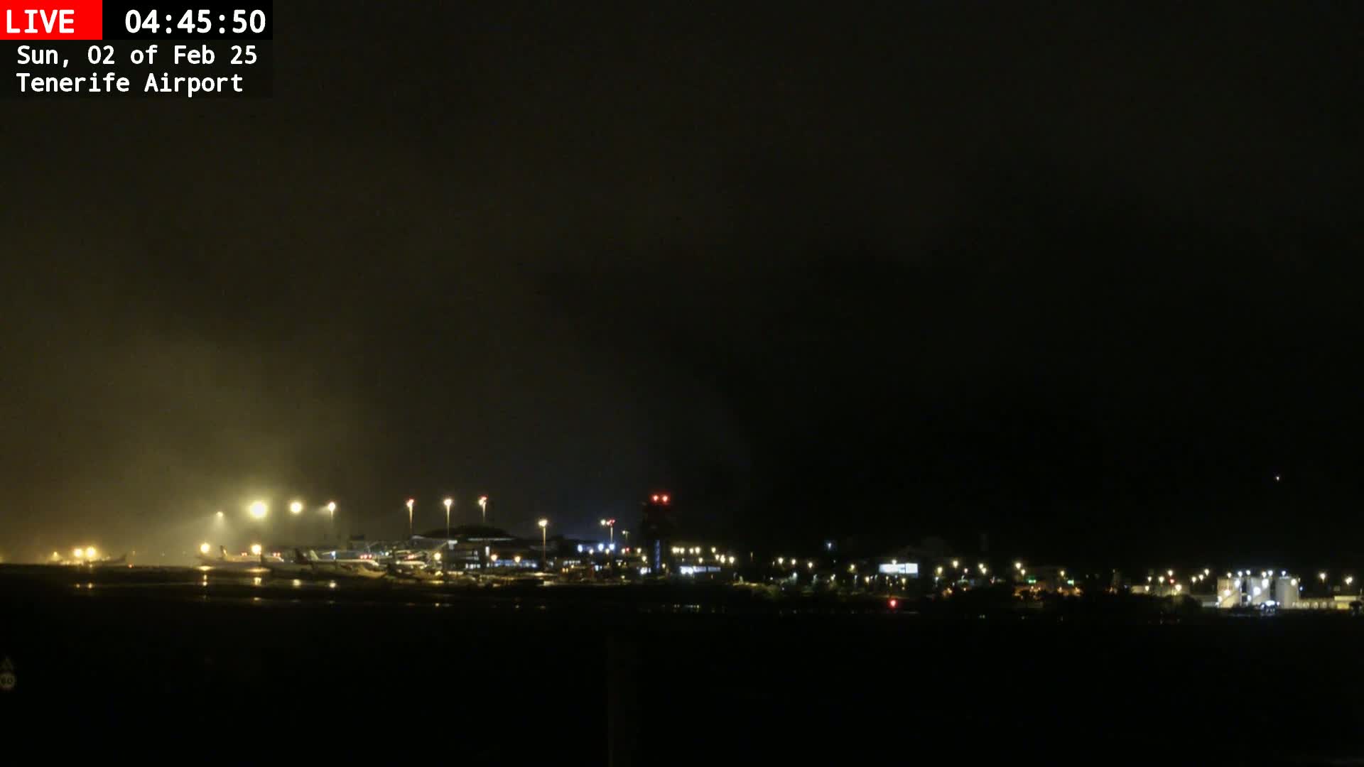 A nighttime view of an airport runway and terminal buildings under a foggy sky.