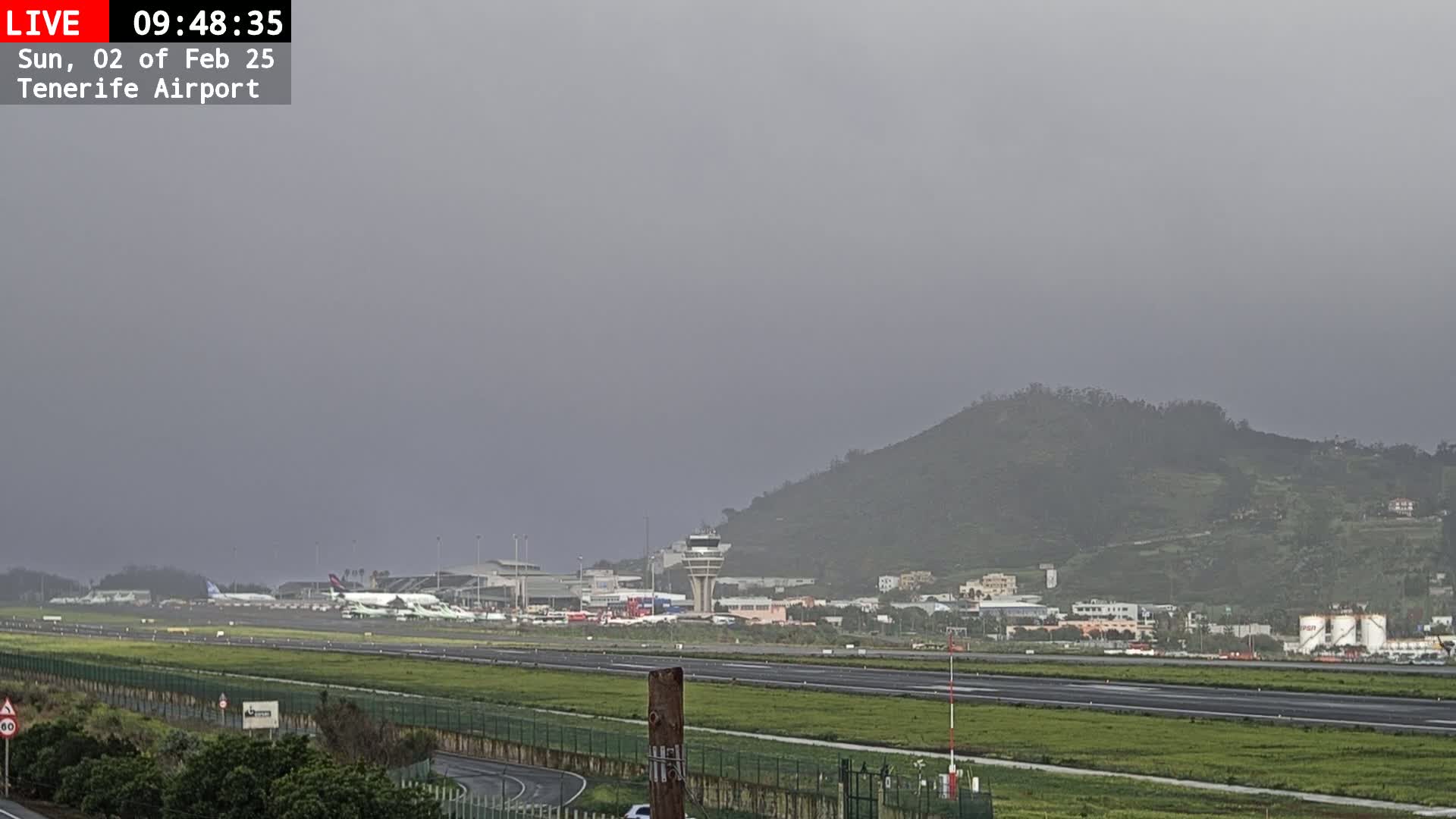 A hazy, overcast day reveals an airport with several airplanes on the tarmac, a control tower, and a hill in the background.