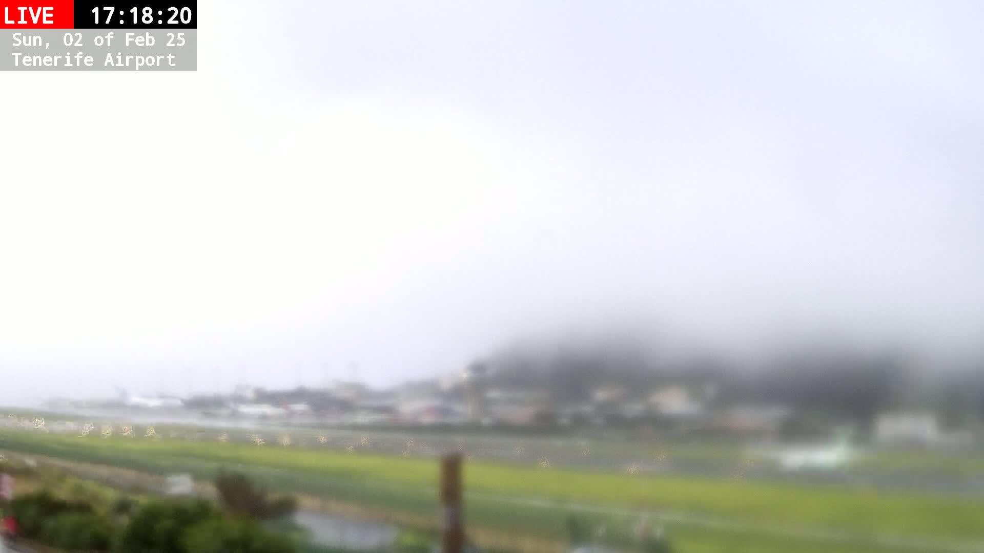 A blurry view of a foggy, rainy landscape shows a field and buildings in the distance.
