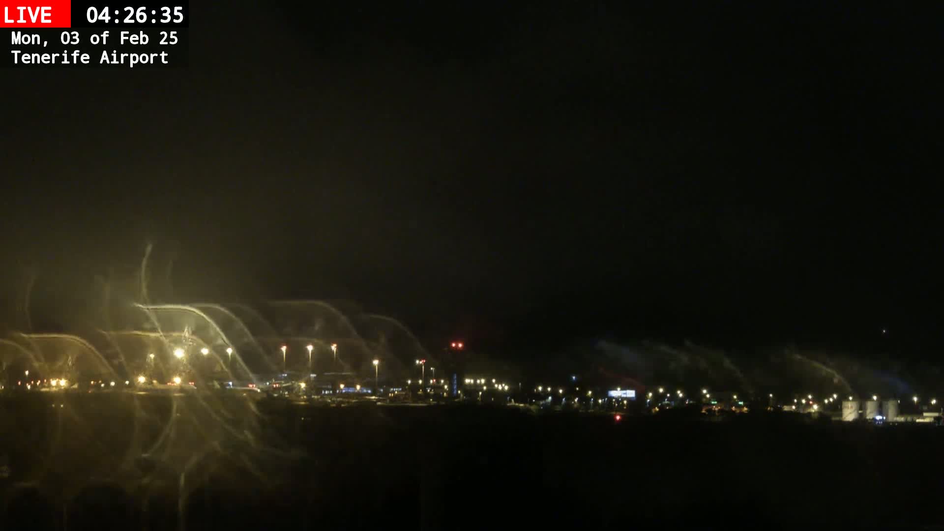 A nighttime view of an airport runway and surrounding area, obscured by a heavy mist or spray.