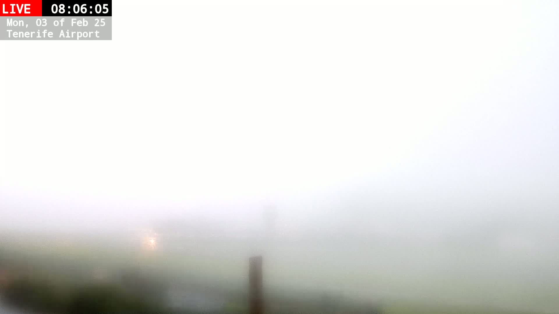 A thick fog obscures the view of a flat, grassy area with a single, dark post visible in the middle ground.