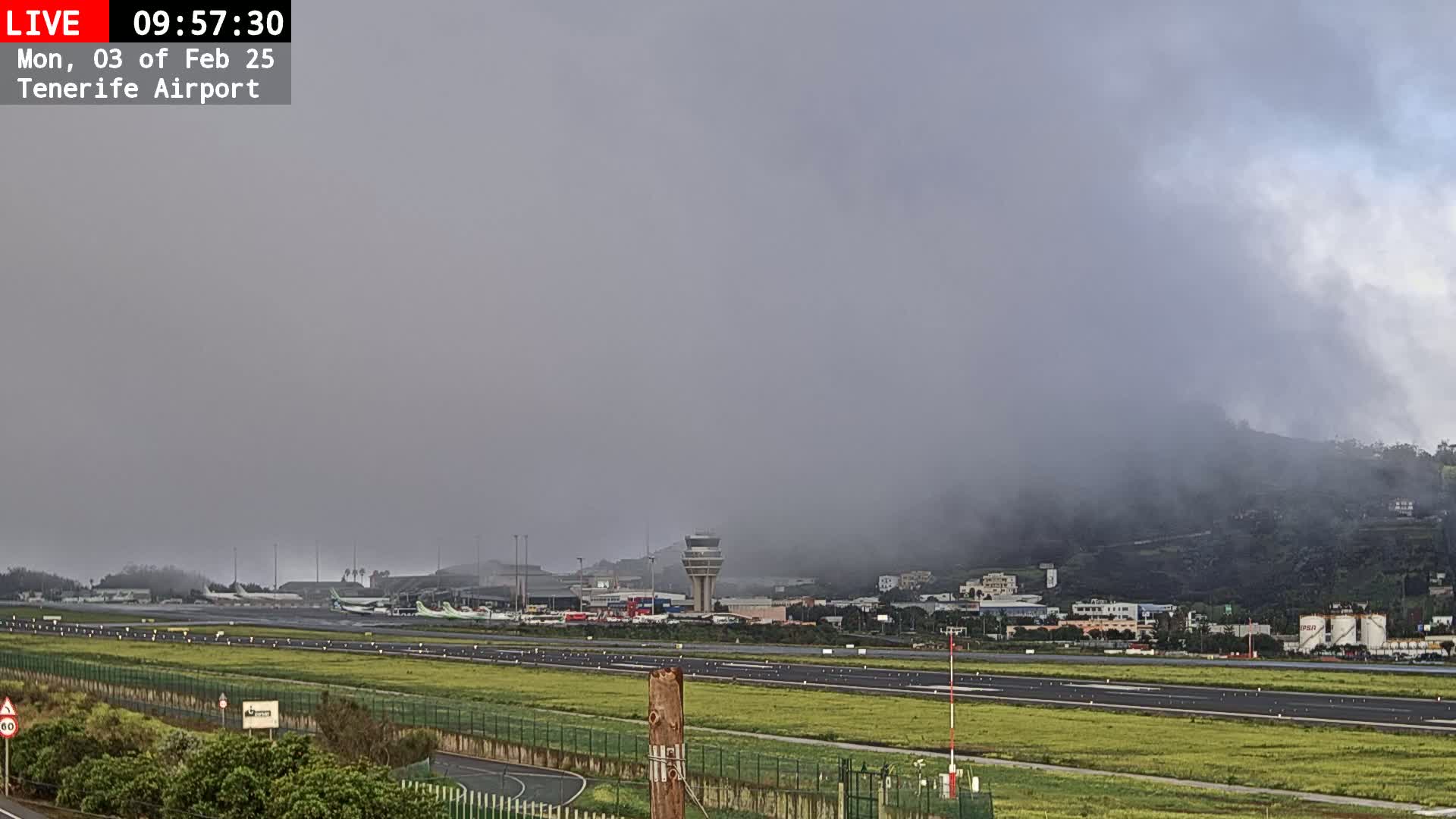 A foggy airport with several planes on the tarmac and a control tower visible in the distance.