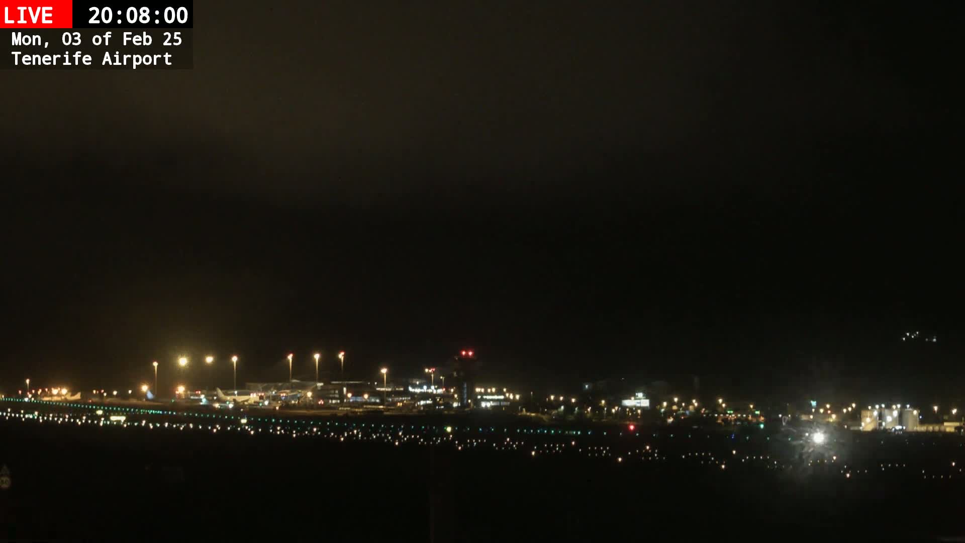 A nighttime view of an airport runway and terminal buildings under a dark, overcast sky.
