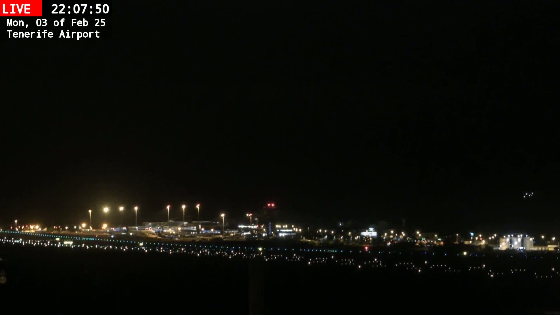 A nighttime view of an airport runway and terminal buildings illuminated under a clear, dark sky.