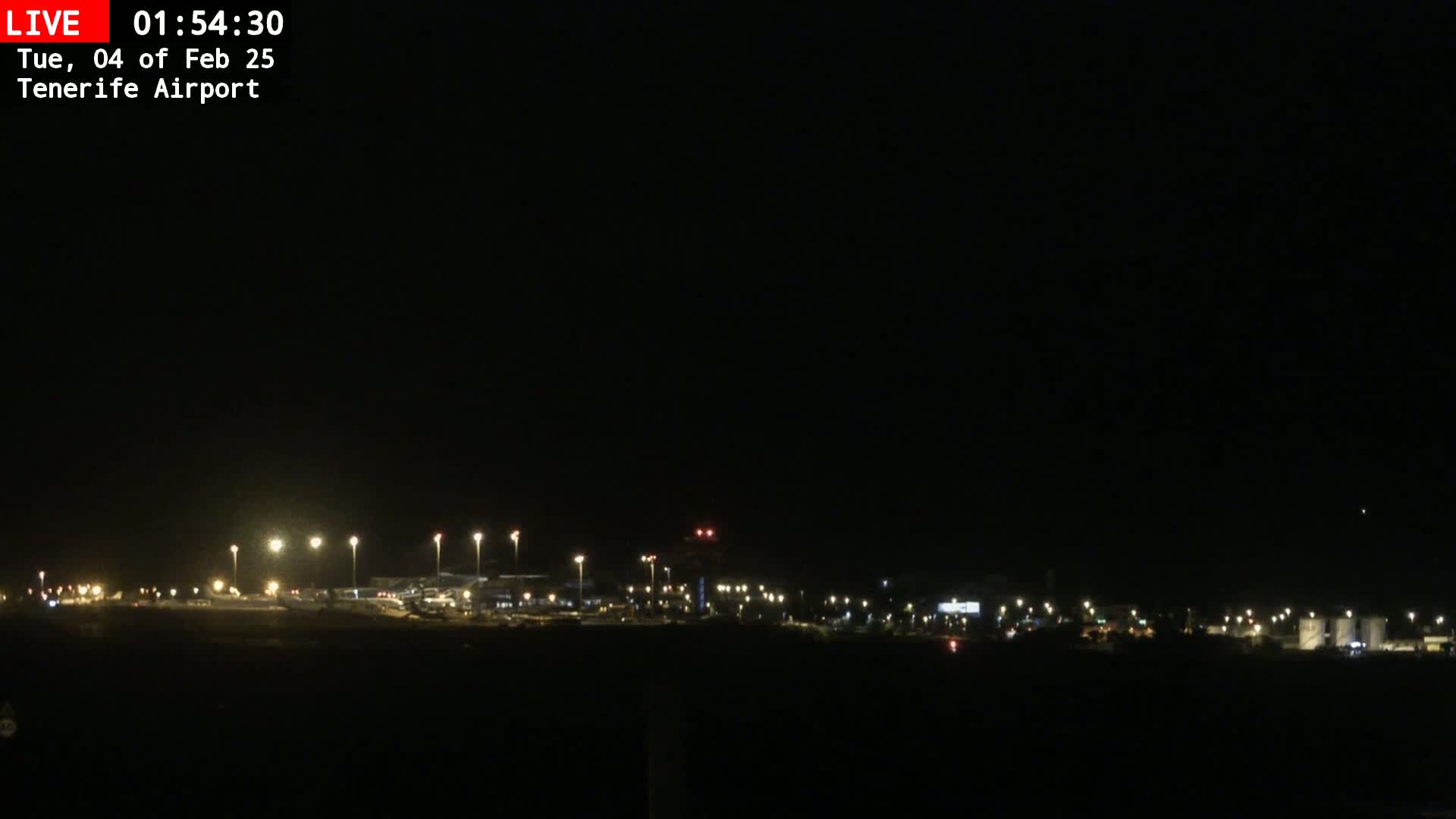 A nighttime view of an airport runway and surrounding buildings illuminated by lights under a clear, dark sky.