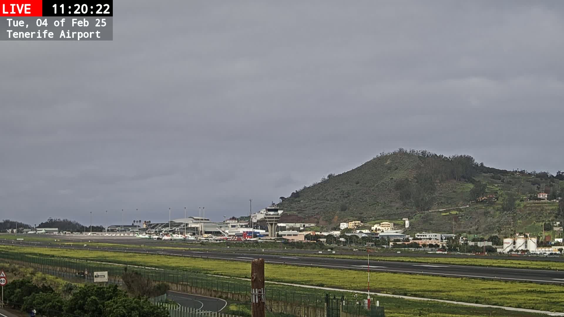 An airport runway stretches towards a low, green hill under an overcast sky.